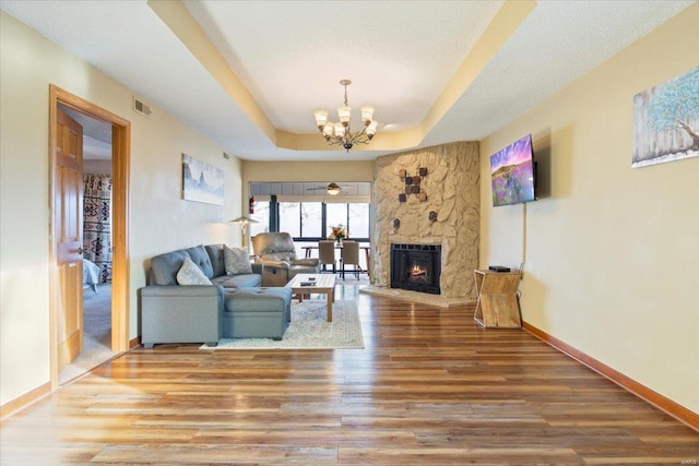 living room with hardwood / wood-style floors, a raised ceiling, a stone fireplace, and an inviting chandelier