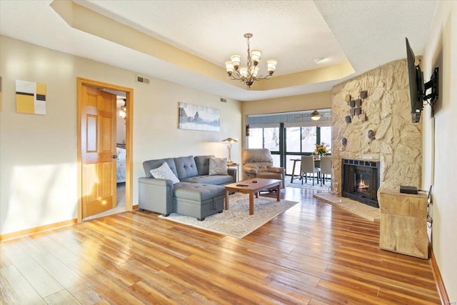 living room featuring a raised ceiling, hardwood / wood-style flooring, an inviting chandelier, and a stone fireplace