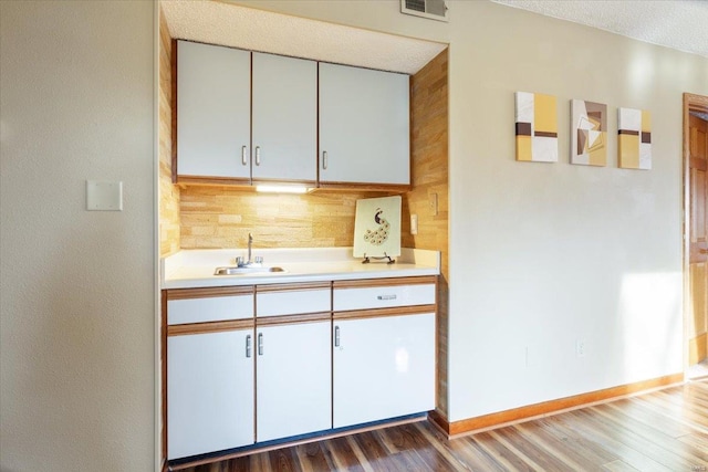 kitchen with white cabinetry, sink, backsplash, hardwood / wood-style floors, and a textured ceiling