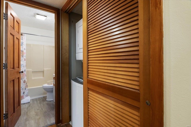 hall with wood-type flooring, a textured ceiling, and stacked washing maching and dryer