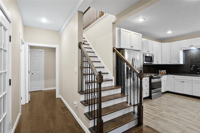 kitchen with appliances with stainless steel finishes, backsplash, light hardwood / wood-style floors, and white cabinetry