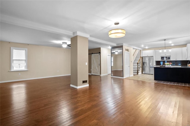 unfurnished living room featuring wood-type flooring, a barn door, and ceiling fan