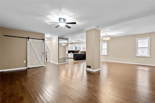 unfurnished living room with dark hardwood / wood-style floors, a barn door, plenty of natural light, and ceiling fan