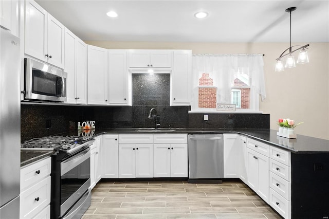 kitchen with white cabinetry, sink, dark stone countertops, decorative light fixtures, and appliances with stainless steel finishes