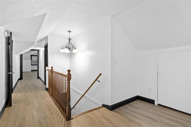 corridor featuring light hardwood / wood-style flooring, vaulted ceiling, and an inviting chandelier