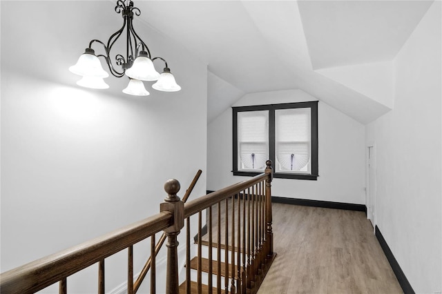 hall with a chandelier, light hardwood / wood-style floors, and vaulted ceiling