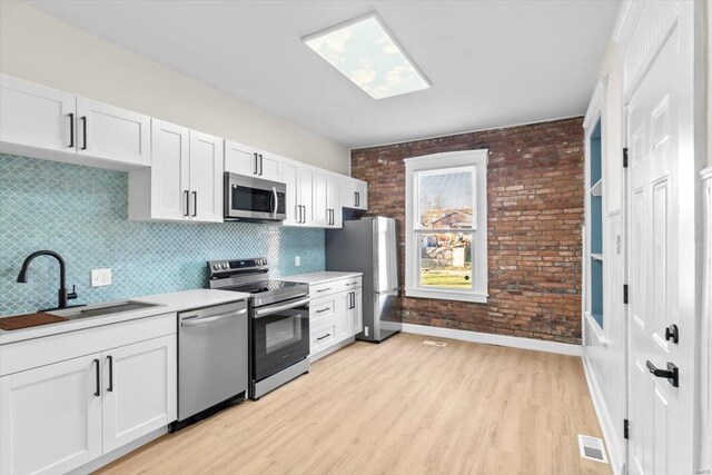 kitchen featuring brick wall, stainless steel appliances, white cabinetry, and sink