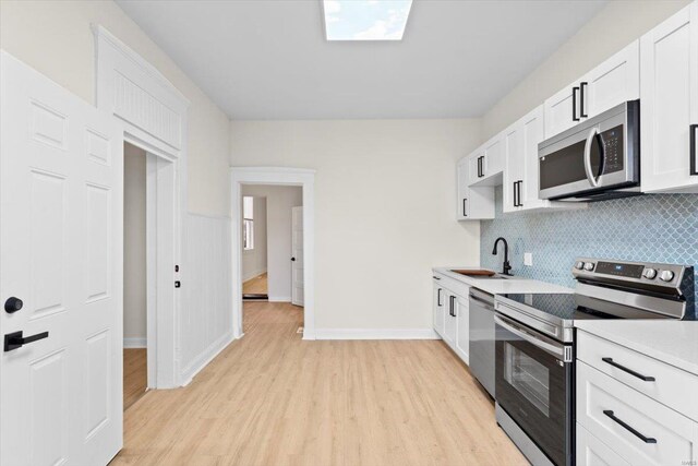 kitchen featuring white cabinetry, sink, tasteful backsplash, light hardwood / wood-style flooring, and appliances with stainless steel finishes