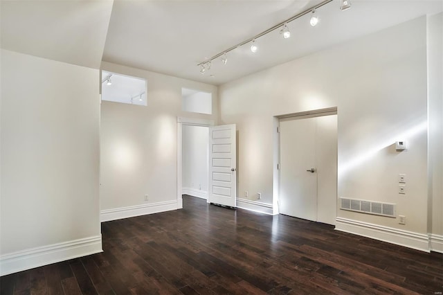 empty room with dark hardwood / wood-style flooring, a towering ceiling, and track lighting