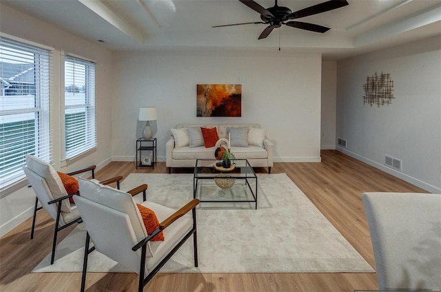 living room featuring a raised ceiling, ceiling fan, and light hardwood / wood-style flooring