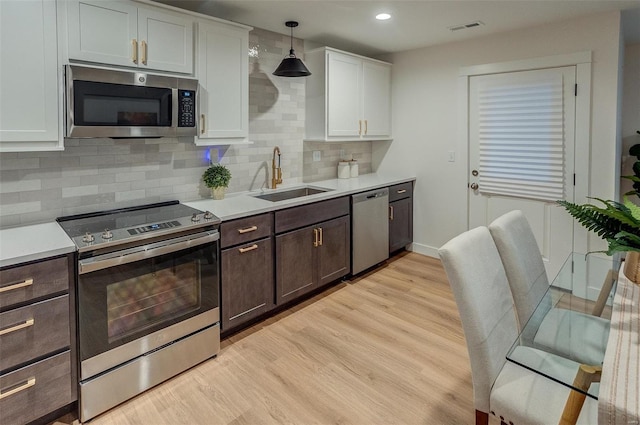 kitchen featuring stainless steel appliances, sink, pendant lighting, light hardwood / wood-style flooring, and white cabinets