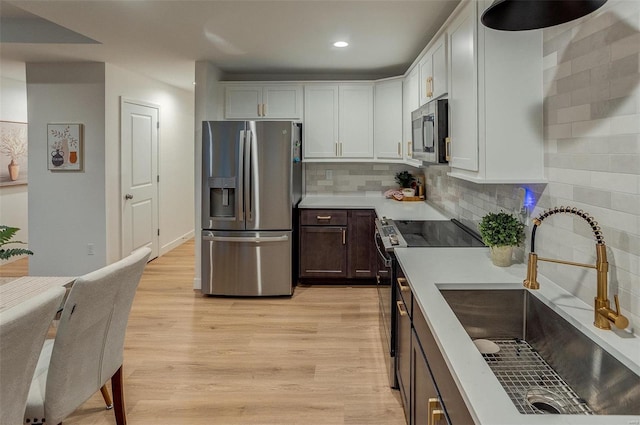 kitchen with backsplash, white cabinets, sink, light wood-type flooring, and stainless steel appliances