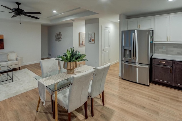 dining area featuring light hardwood / wood-style floors, ceiling fan, and a tray ceiling