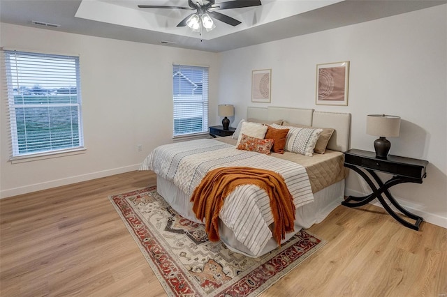 bedroom with a raised ceiling, light hardwood / wood-style flooring, and ceiling fan