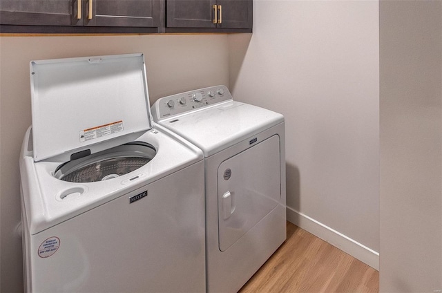 laundry area featuring washer and clothes dryer, light hardwood / wood-style floors, and cabinets