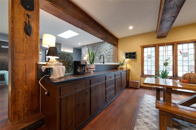 kitchen with beam ceiling, dark brown cabinetry, and dark wood-type flooring