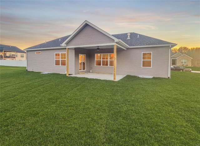 back house at dusk featuring a lawn, ceiling fan, and a patio