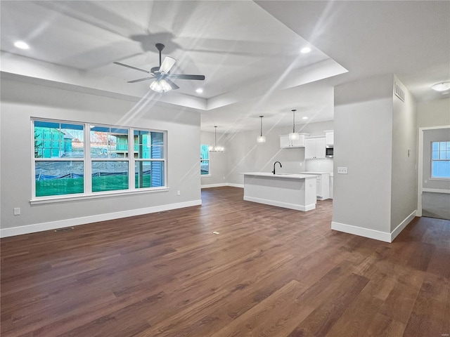 unfurnished living room with dark hardwood / wood-style floors, a healthy amount of sunlight, sink, and ceiling fan with notable chandelier