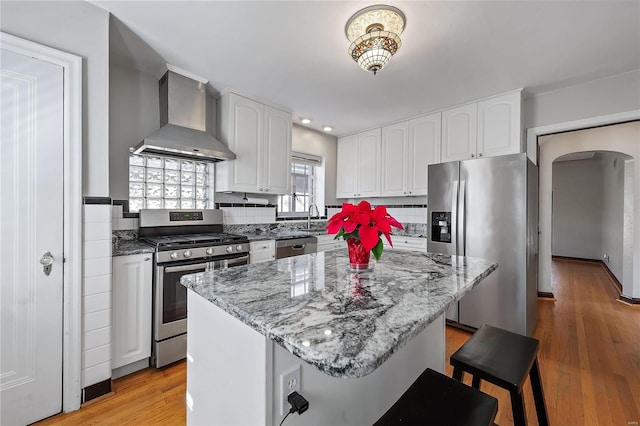 kitchen with a center island, light wood-type flooring, wall chimney range hood, and stainless steel appliances