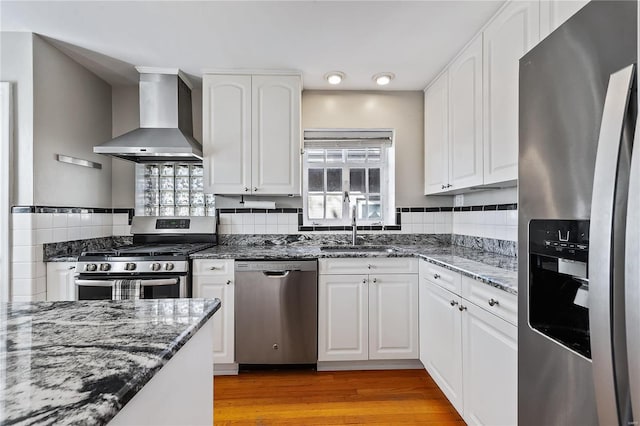 kitchen featuring white cabinetry, stainless steel appliances, wall chimney range hood, and light hardwood / wood-style floors