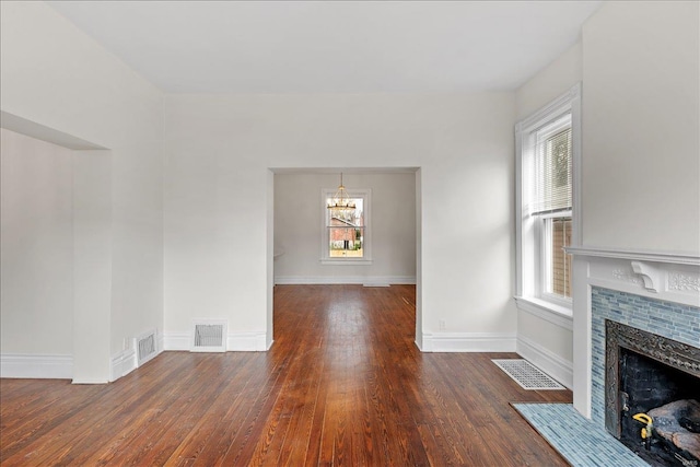 unfurnished living room with a healthy amount of sunlight, dark wood-type flooring, and a tiled fireplace