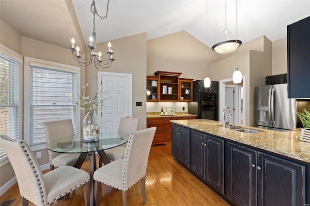 dining area featuring sink, light hardwood / wood-style floors, vaulted ceiling, and an inviting chandelier