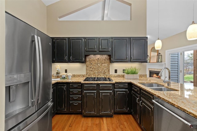 kitchen with sink, stainless steel appliances, light stone counters, pendant lighting, and decorative backsplash