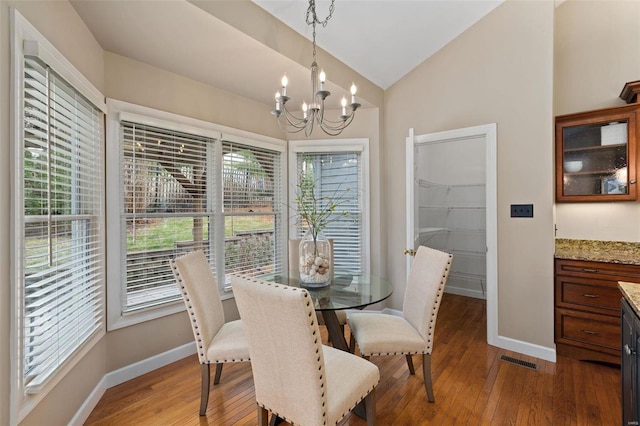 dining area featuring hardwood / wood-style floors, vaulted ceiling, and an inviting chandelier