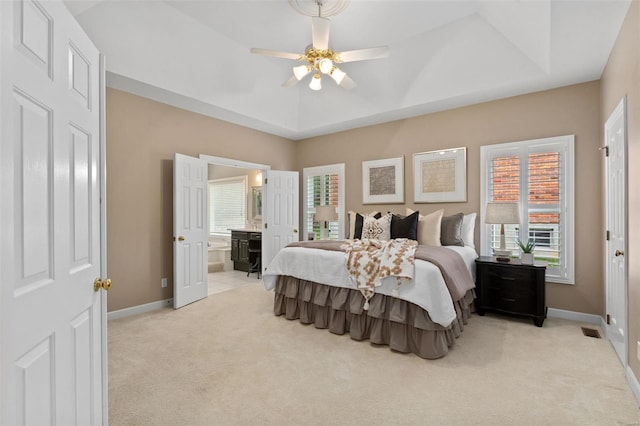 bedroom featuring ceiling fan, a raised ceiling, light colored carpet, and ensuite bathroom