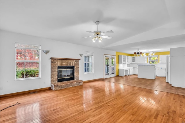 unfurnished living room featuring a fireplace, light wood-type flooring, vaulted ceiling, and ceiling fan with notable chandelier