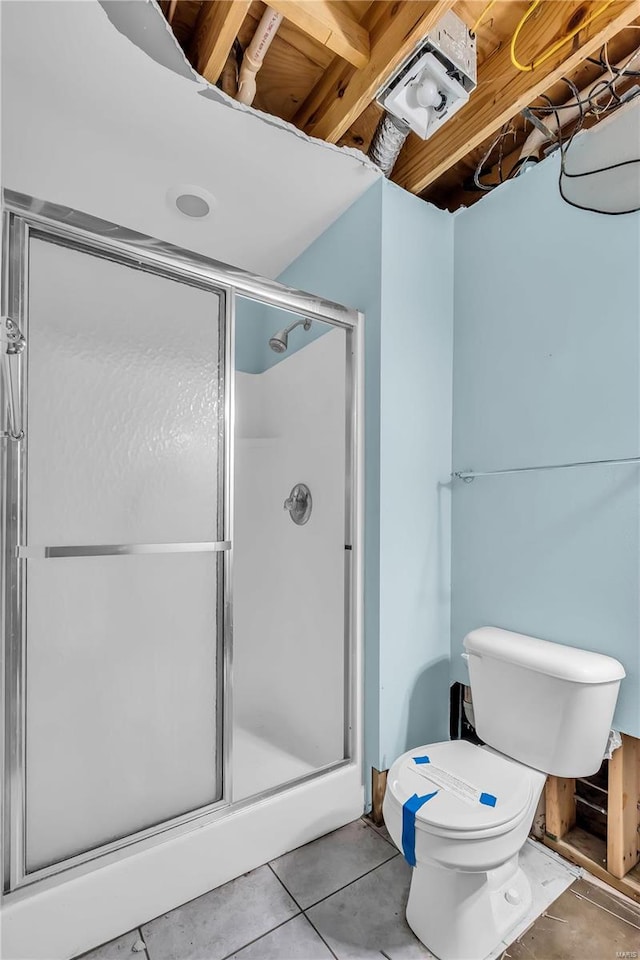 bathroom with tile patterned floors, toilet, and a shower with door