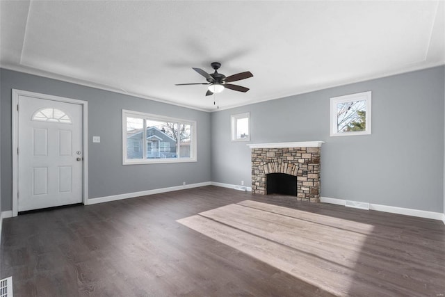 unfurnished living room with a stone fireplace, dark wood-type flooring, ornamental molding, and ceiling fan