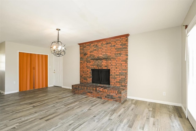 unfurnished living room featuring hardwood / wood-style floors, a notable chandelier, and a brick fireplace