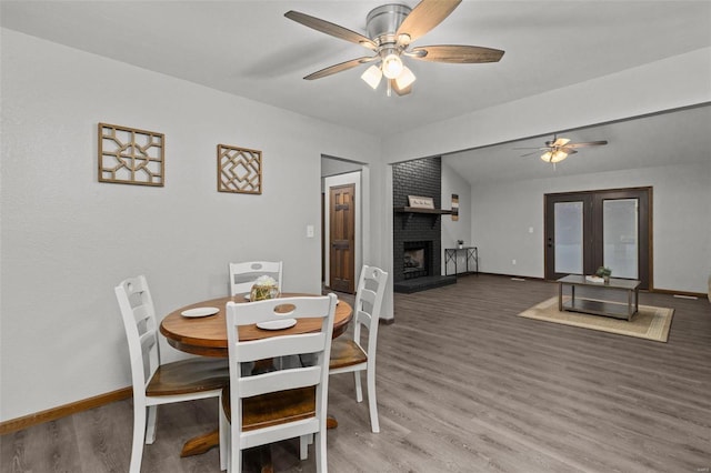 dining space with ceiling fan, wood-type flooring, and a brick fireplace