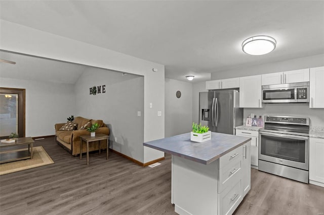 kitchen featuring stainless steel appliances, white cabinets, lofted ceiling, a kitchen island, and hardwood / wood-style flooring