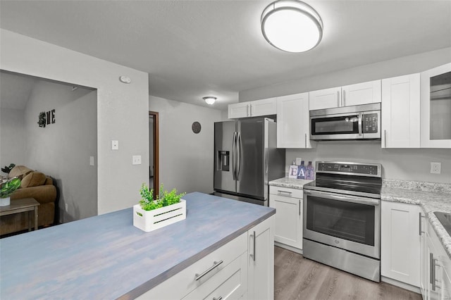 kitchen with light wood-type flooring, stainless steel appliances, white cabinetry, and light stone counters