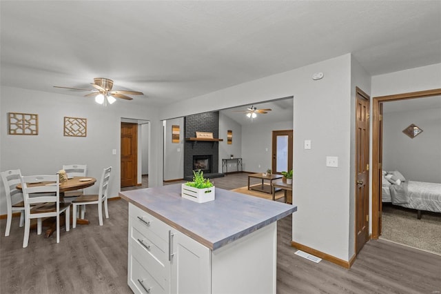 kitchen with white cabinetry, light hardwood / wood-style flooring, ceiling fan, and a brick fireplace