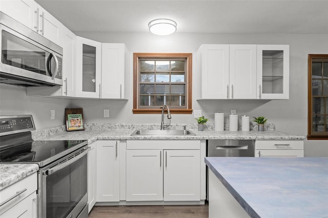 kitchen with white cabinets, sink, hardwood / wood-style flooring, light stone countertops, and appliances with stainless steel finishes