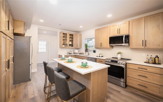 kitchen with appliances with stainless steel finishes, light brown cabinetry, a kitchen bar, a center island, and light hardwood / wood-style floors