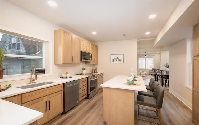 kitchen with light brown cabinetry, sink, a kitchen bar, a center island, and stainless steel appliances