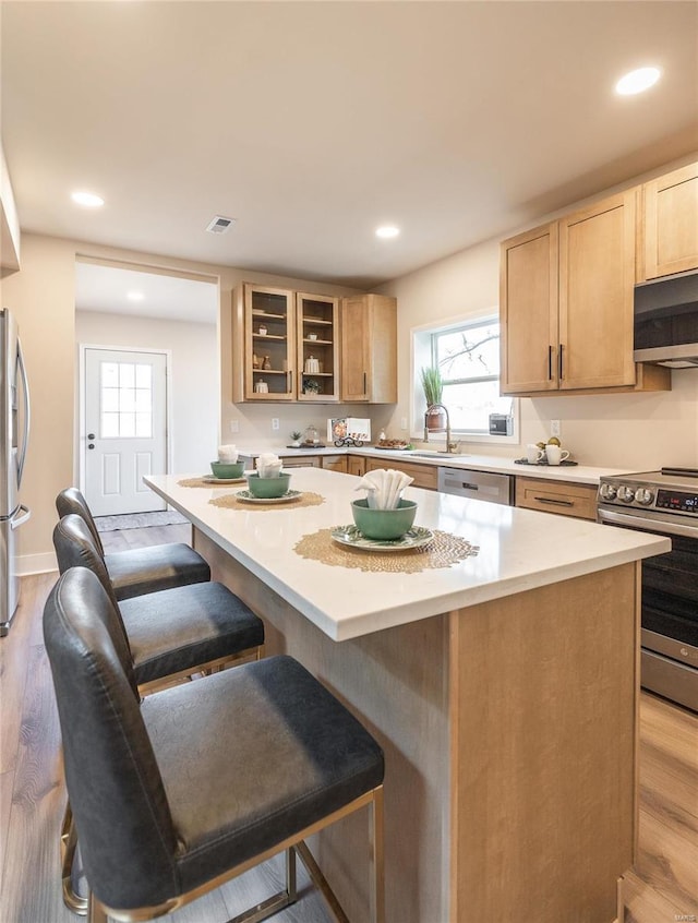 kitchen with sink, a kitchen breakfast bar, a center island, stainless steel appliances, and light brown cabinets