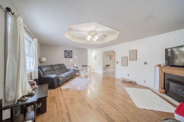 living room featuring a raised ceiling, ceiling fan, light hardwood / wood-style floors, and a textured ceiling