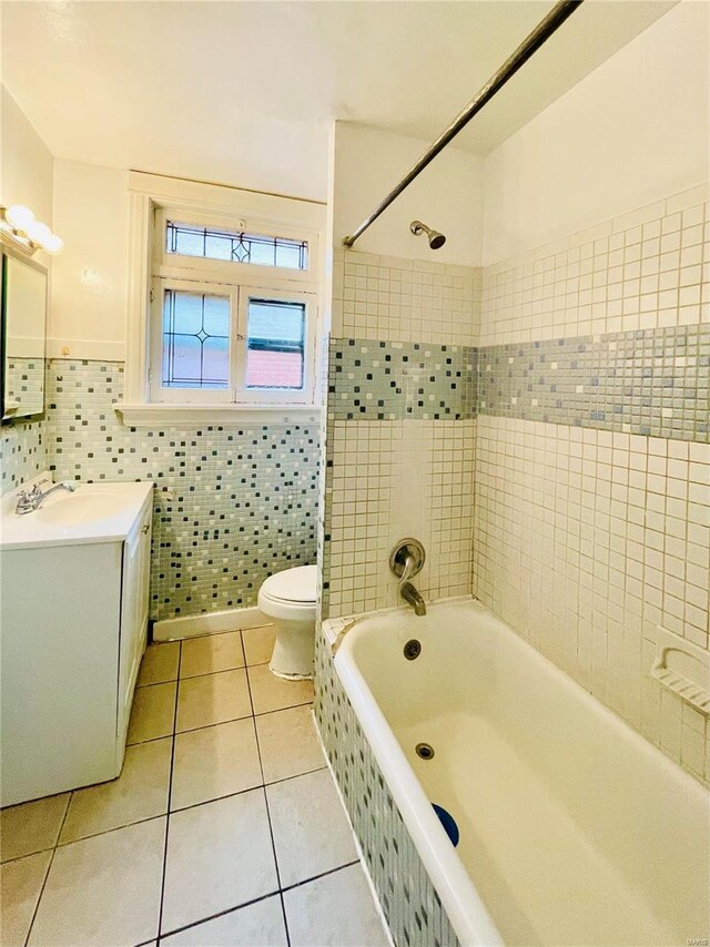 full bathroom with tiled shower / bath combo, tile patterned flooring, toilet, vanity, and tile walls