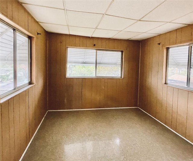 spare room with a healthy amount of sunlight, a paneled ceiling, and wooden walls