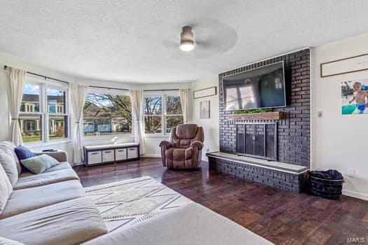 living room with ceiling fan, dark hardwood / wood-style flooring, a textured ceiling, and a brick fireplace