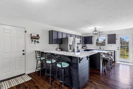 kitchen with dark wood-type flooring, a notable chandelier, kitchen peninsula, stainless steel fridge, and a kitchen bar