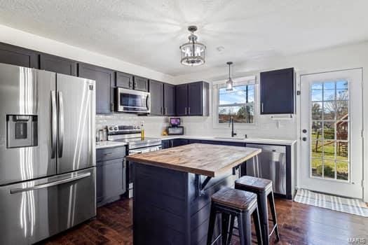 kitchen with a center island, a breakfast bar area, dark hardwood / wood-style floors, decorative light fixtures, and stainless steel appliances