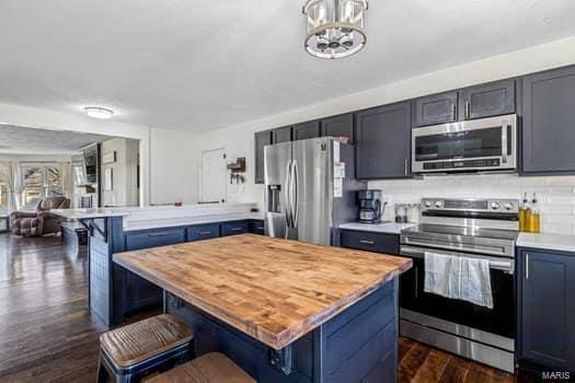 kitchen with a center island, dark wood-type flooring, a breakfast bar area, decorative backsplash, and stainless steel appliances