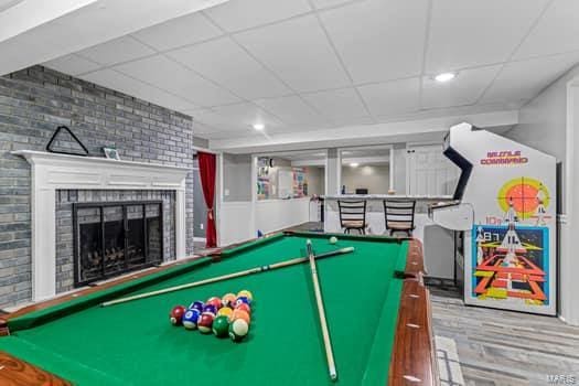 recreation room featuring a brick fireplace, a drop ceiling, brick wall, hardwood / wood-style floors, and pool table