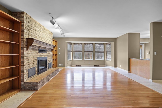 unfurnished living room featuring a fireplace, light hardwood / wood-style floors, and track lighting